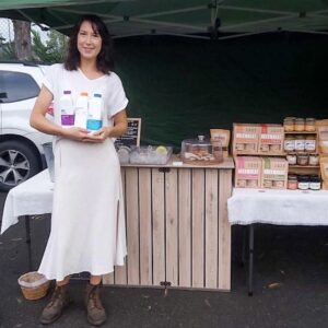 An image of a lady holding up bottles of Nutmylk in front of market stand